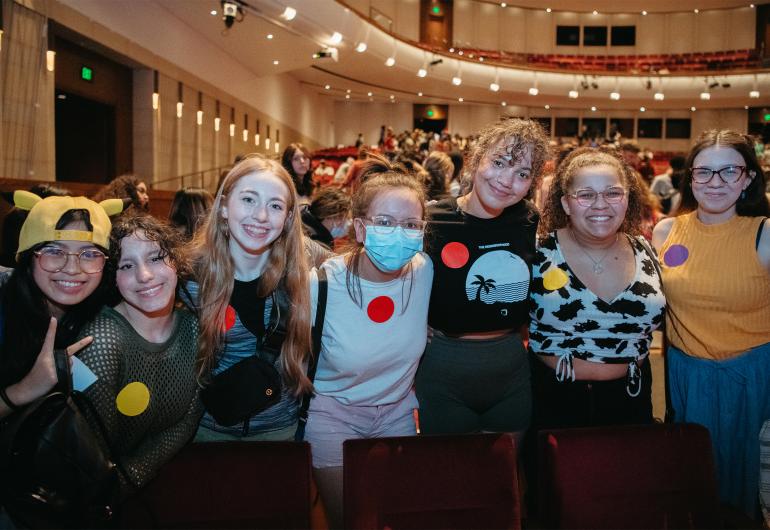 A group of female students standing in the Northrop theater smile for the camera.