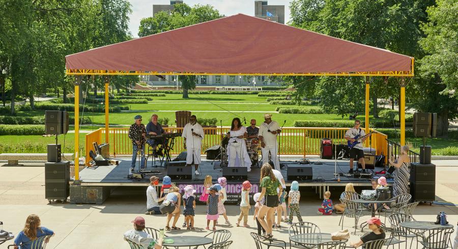 Musical group Funktion Junction plays on the Northrop Plaza stage for audience members outside. A group of children stand right in front of the stage. 
