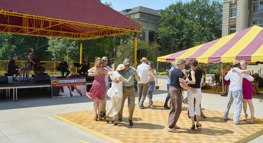 Audience members dance in pairs on a dance floor outside while live musicians accompany them on the Northrop Plaza Stage.