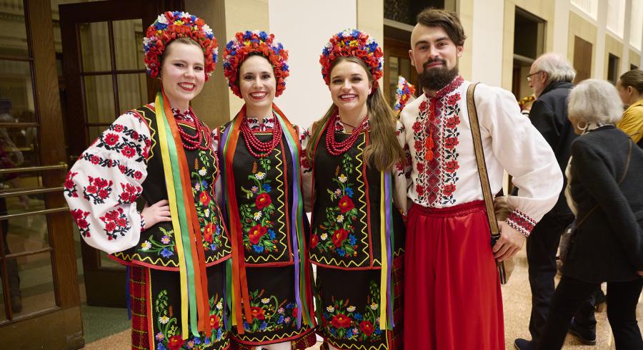 Four people wearing brightly colored traditional Ukrainian dress face the camera and smile.