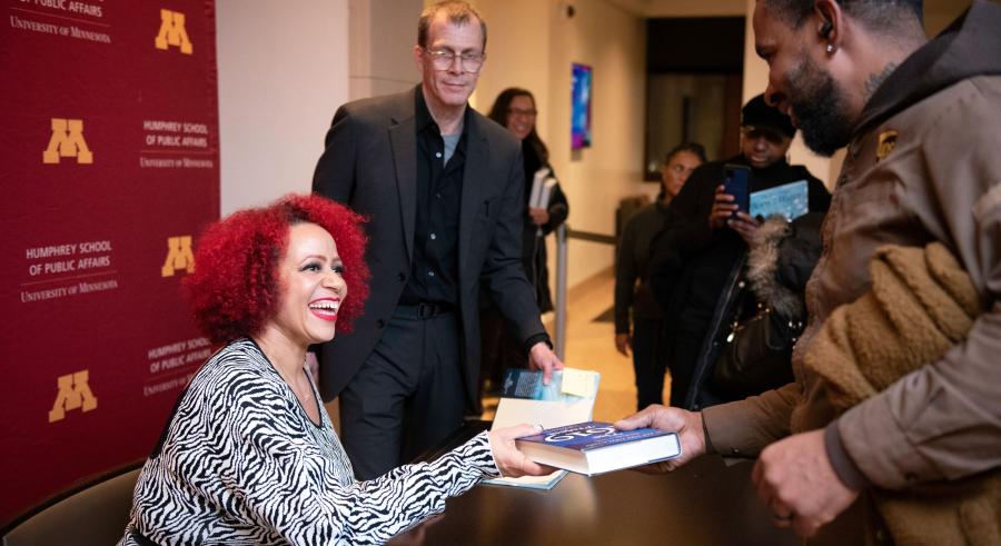 Nikole Hannah-Jones signing a patron’s book while smiling. Other patrons stand behind with their own copies of the book.