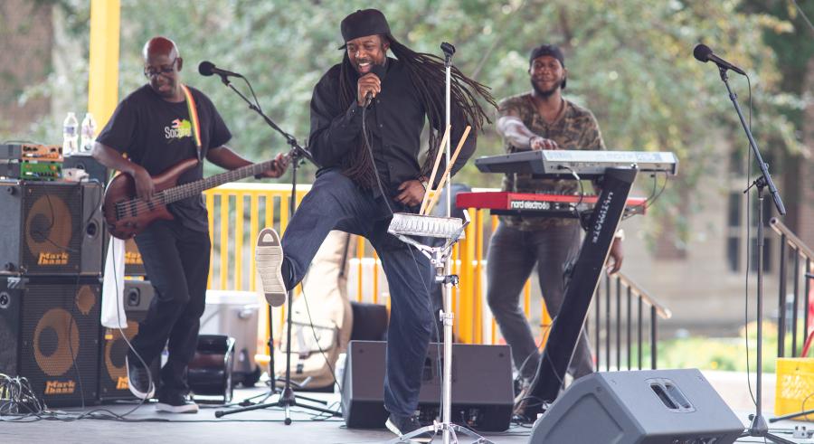 Three musicians making up Socaholix performing on the Northrop Plaza Stage. From left to right, they are playing guitar, singing, and playing the keyboard.