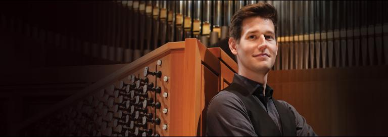 Greg Zelek, Northrop’s new organist, sitting at the organ. Zelek is wearing a dark long-sleeved shirt and a vest.