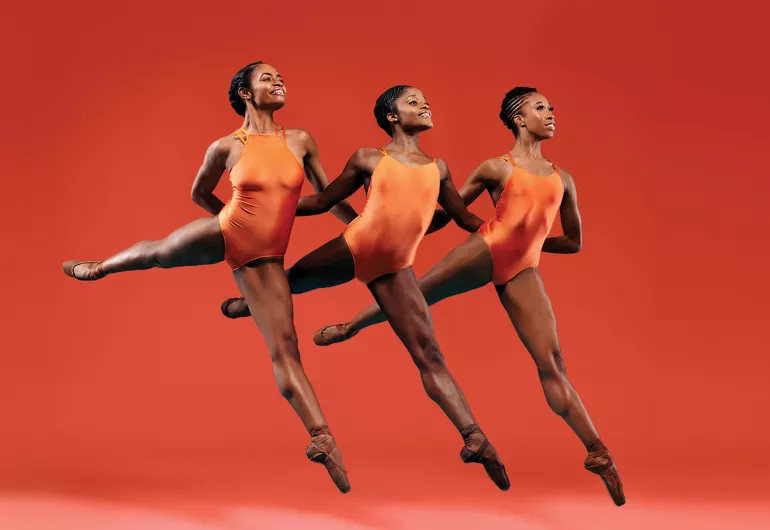 Three female dancers perform together in front of an orange background.