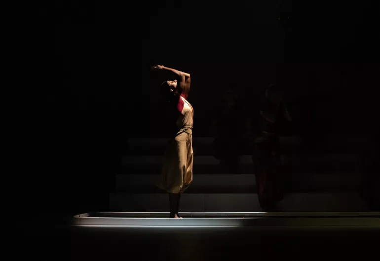 Dancer stands in a pool, hand cupped over her head letting water fall behind her