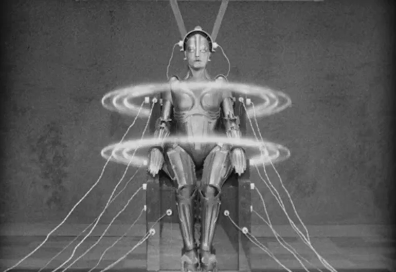 A human-like figure sits in a chair with wires connected to it. Two large circles float around the shoulders and waist of the figure. 