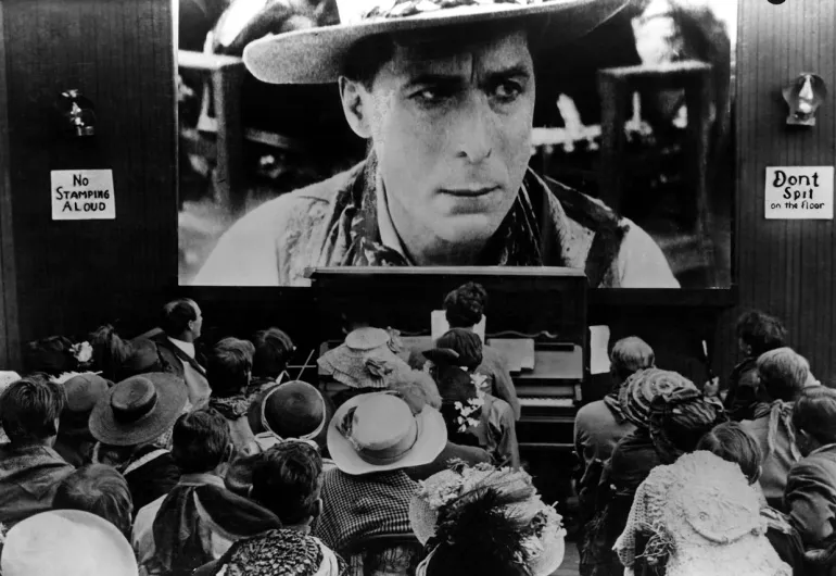 Historical image of a screening of a silent film with organist and audience facing the screen.