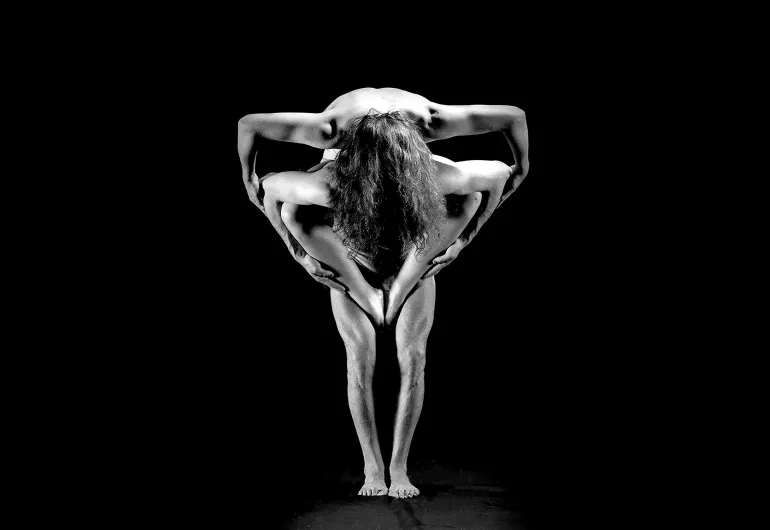 A black and white image depicts two dancers contorted to form a triangle with their arms and legs.