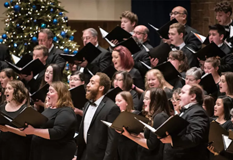 A large choir in formal attire singing from songbooks.