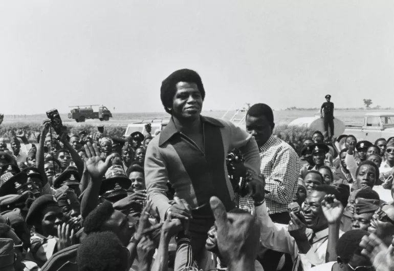 Historical image of a crowd of cheering black men. Two men are raised above the crowd.