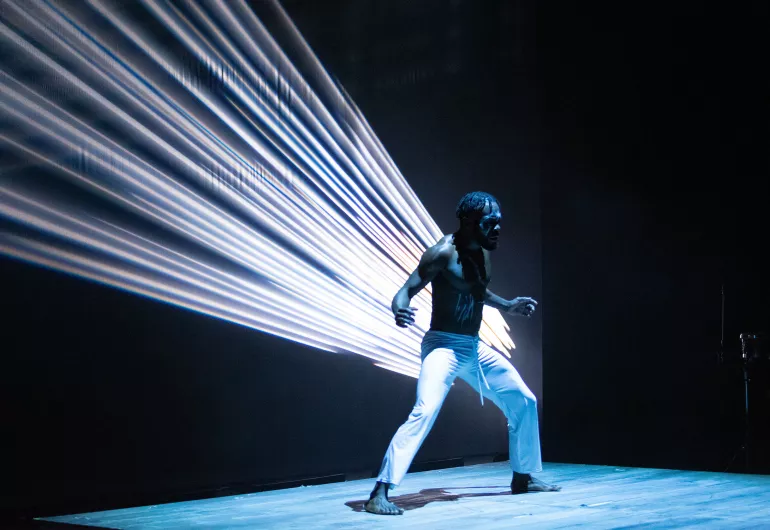 Step Afrika! dancer with rays of light projected behind him