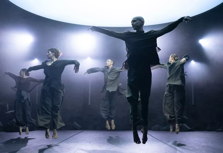 Ballet Met company members jumping straight up with arms out to sides and heads turned to their right