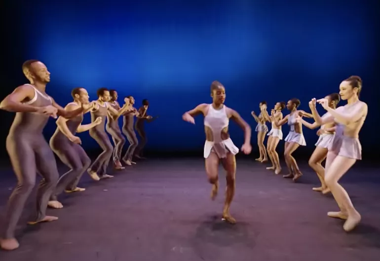 Video still of dancers lined on either side of a dancer running through the middle