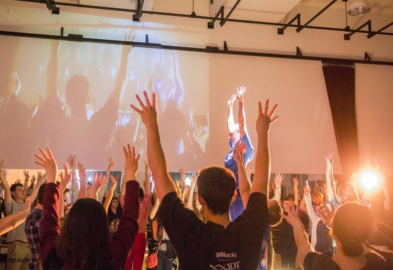 Crowd dances with arms in the air in a white room with projections and lights