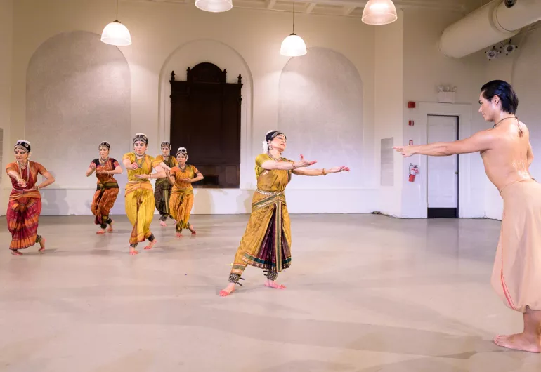 Dancer in white reaches toward a dancer in yellow garb. Other performers run stage right.