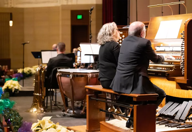 Two people sit side by side playing the organ.