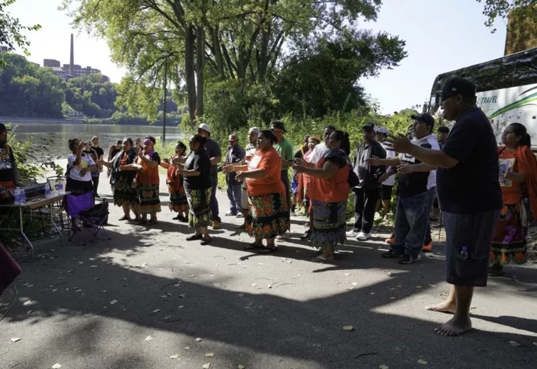 Group of people ceremoniously gathered by a river clapping