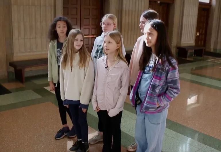 Group of young students standing together attentively in a spacious indoor hall.