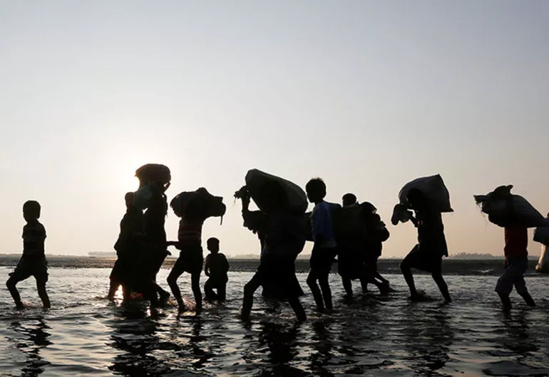 People walking through shallow water carrying belongings