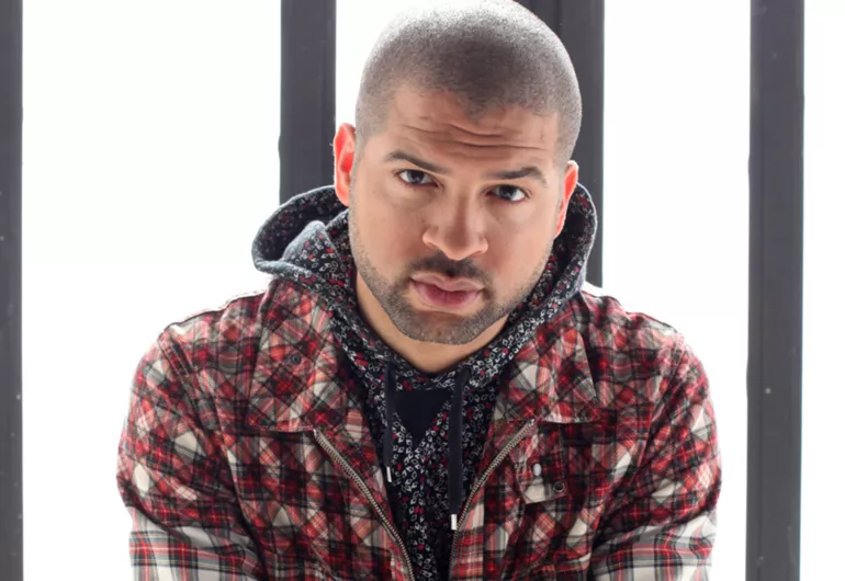 Jason Moran in front of a white and gray background, looking into the camera. 