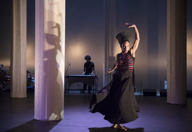 A female dancer performs on stage in front of white columns.