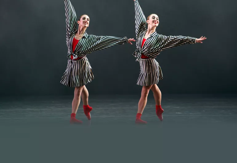 2 American Ballet Theatre dancers in black and white striped dresses over red leotards and red pointe shoes