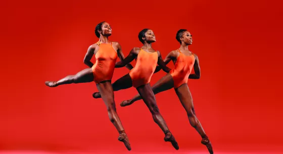 Three woman dancers from DTH in orange leotards leaping through the air in unison 