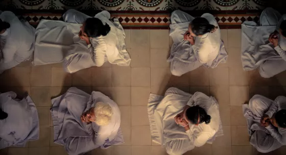 Image of people on the floor in rows legs crossed and hands folded in prayer