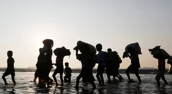 People walking through shallow water carrying belongings