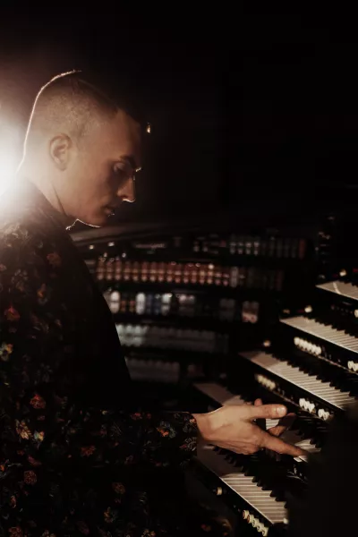 Cameron sitting in profile at the organ with a bright light just over his far shoulder.