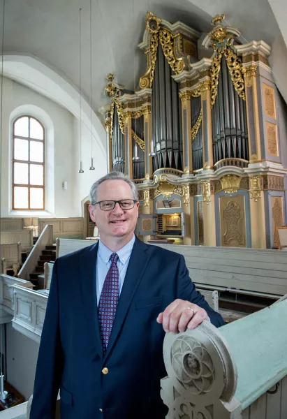 Dean smiling in front of organ pipes with a window behind him.