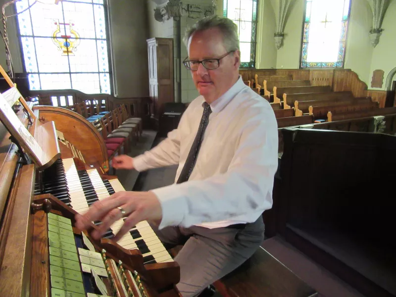 Dean playing an organ with bright windows behind him.