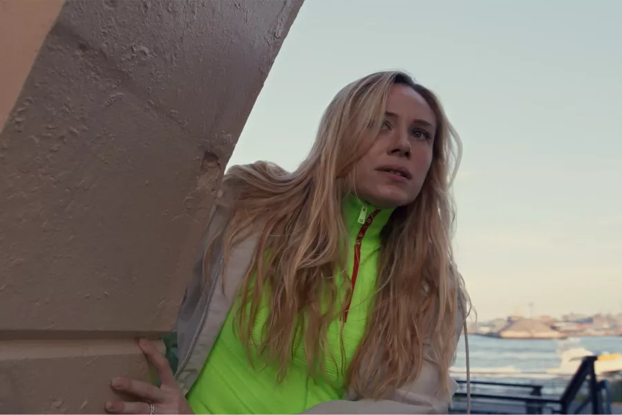 A woman with long blonde hair looks around a stone pillar.