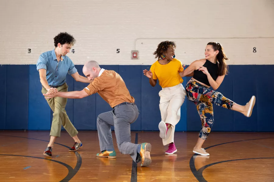 Four dancers perform together in a gymnasium setting.