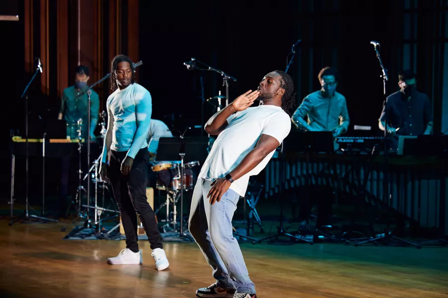 Two dancers on a stage with percussionists behind them.