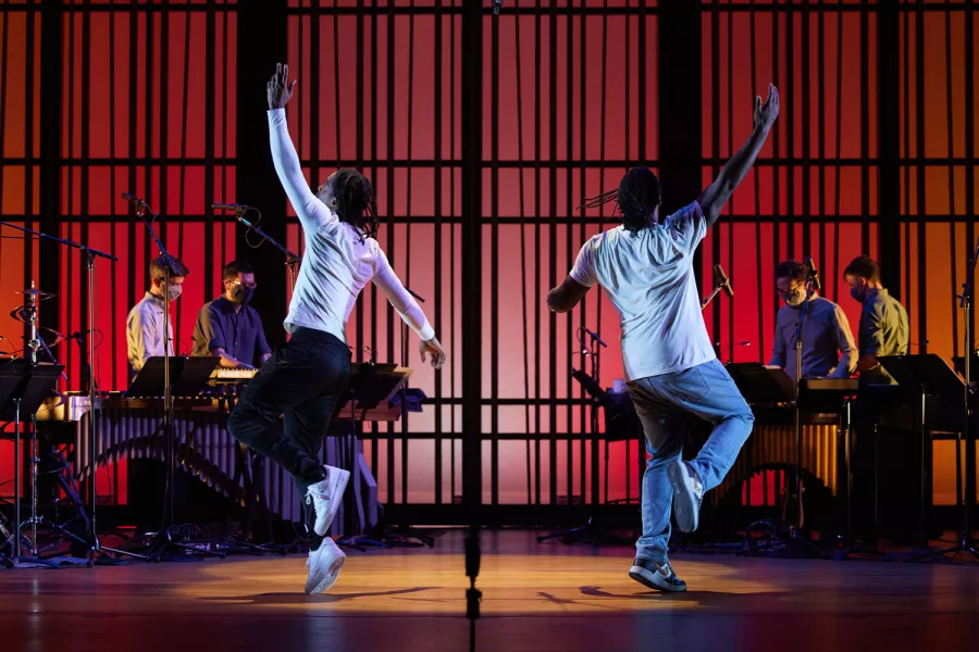 Two dancers on a stage with percussionists behind them.