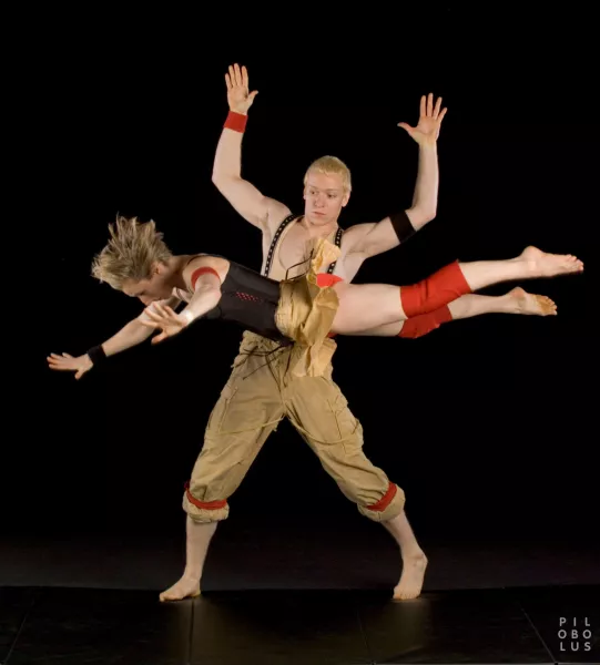 One person stands with their hands in the air staring at a person in front of their torso who appears to be suspended in the air.