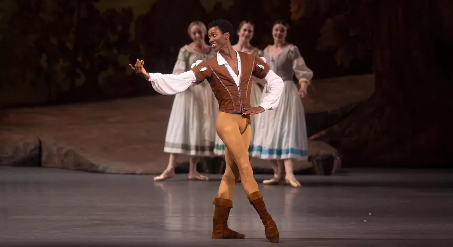 Male dancer in brown villager costume poses center stage.