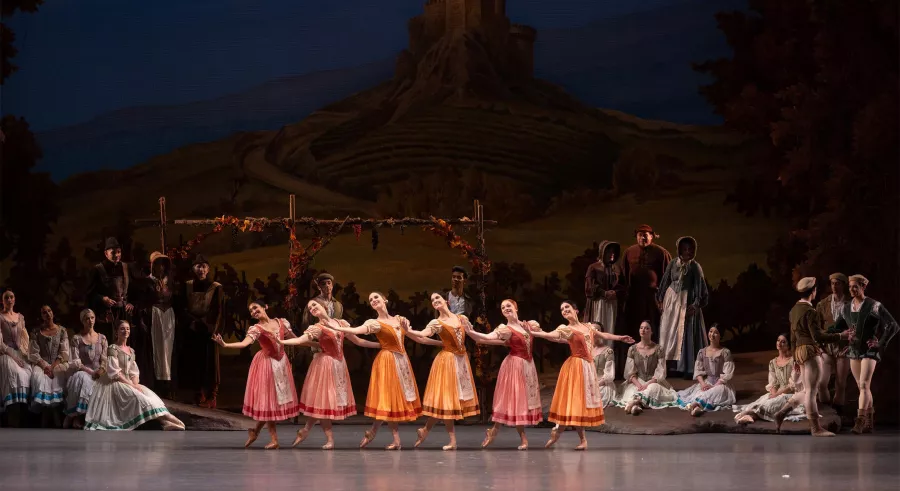 Ballerinas perform in a unison line wearing colorful villager costumes.