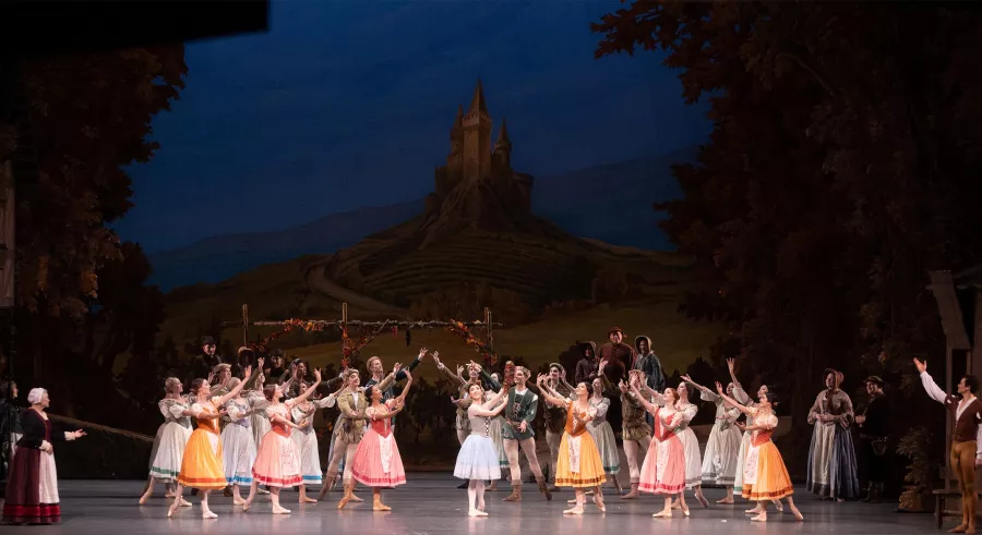 Dancers perform together on a set with a large tower in the distance.