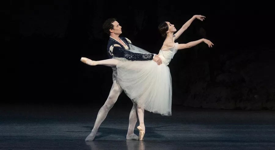 A man and woman dancer pair perform on a dark stage.