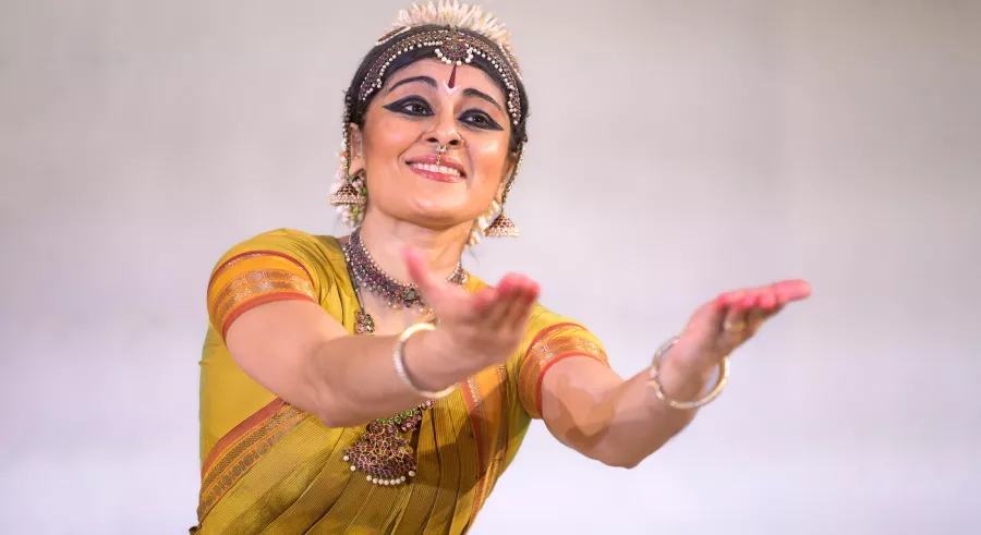 Dancer in traditional make-up and costume reaches out toward camera with both arms.