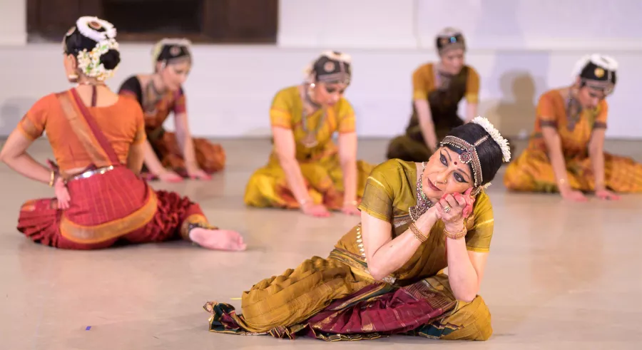 Foremost dancer emotes in a floor pose. Five dancers sit behind her.