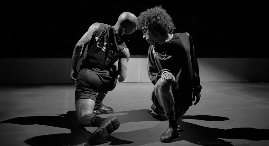 Two dancers kneel, and twist to press their foreheads together.