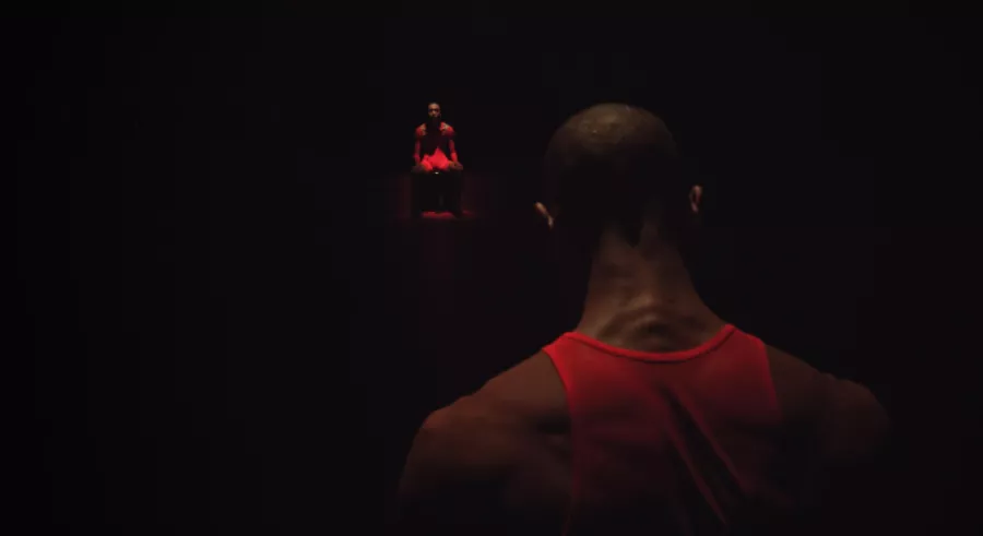 Up-close picture of the back of a man's head, neck, and shoulders. He wears a red shirt and faces something glowing red in the dark.