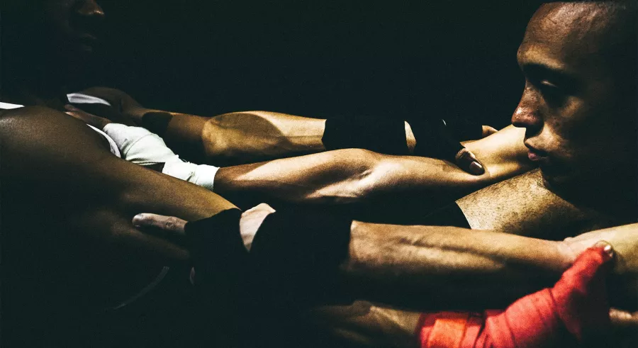 Two men stare at each other from across their grappling arms and gripped hands.