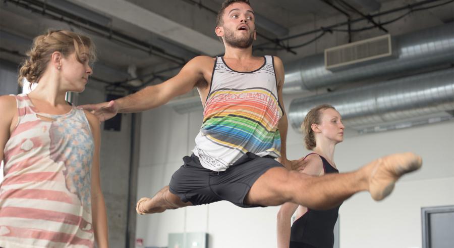 Dancer leaps waist high in the splits splits between two dancers.