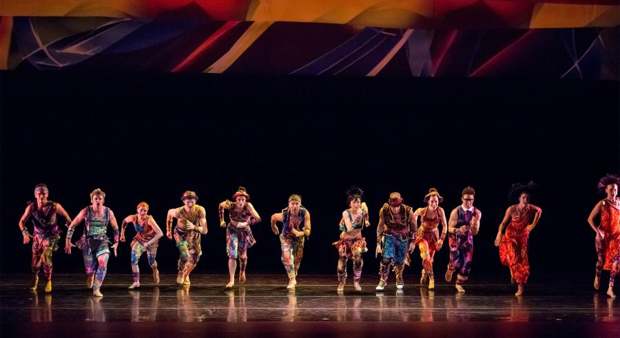 Dancers run forward in a line from upstage center, during a live performance.