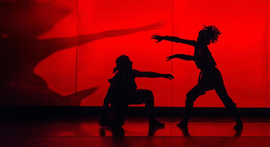 Silhouettes of dancers strike dramatic poses against a glowing red backdrop.