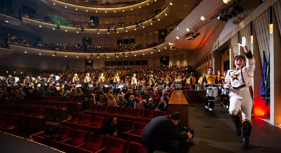 A conductor leads an energetic procession of drummers on stage.